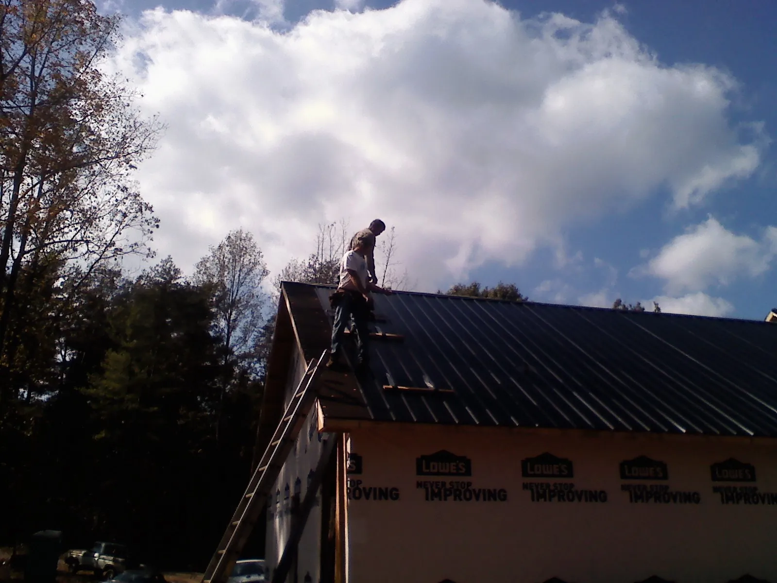 Roofer fastening dark metal panels high against a cloudy sky, from a Roof Inspection job in Nortonville