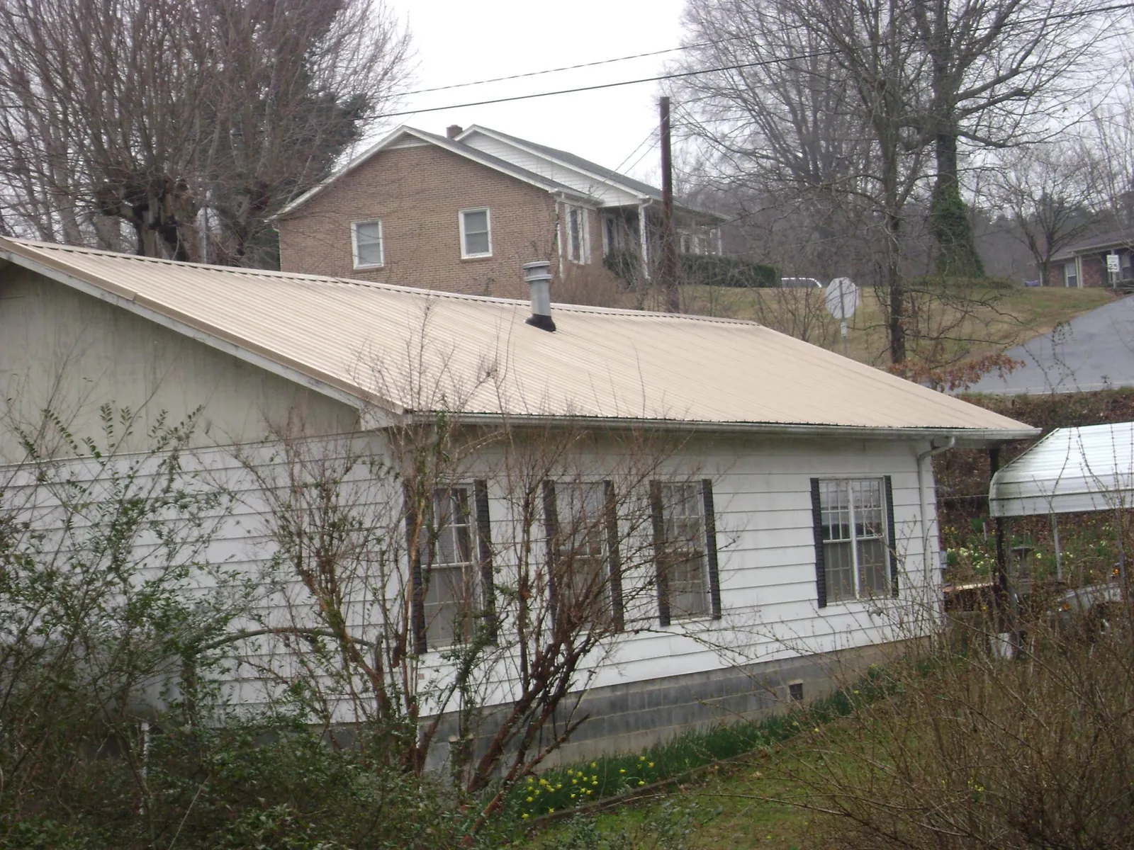 Tan metal roof on a white sided house set into a hillside — Commercial Roofing by Roofing Brothers in Nortonville